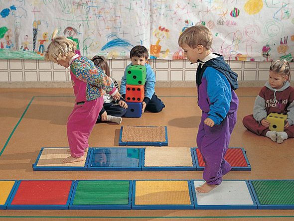 Niños pasando por encima de diferentes elementos cuadrados que tienen diferentes texturas.